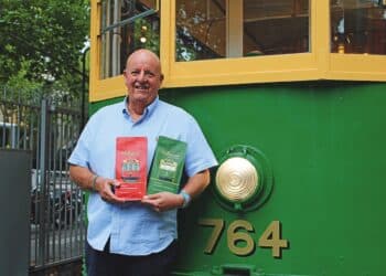 Lance Brown with Melbourne Coffee Group bags posed in front of an historic Melbourne team.